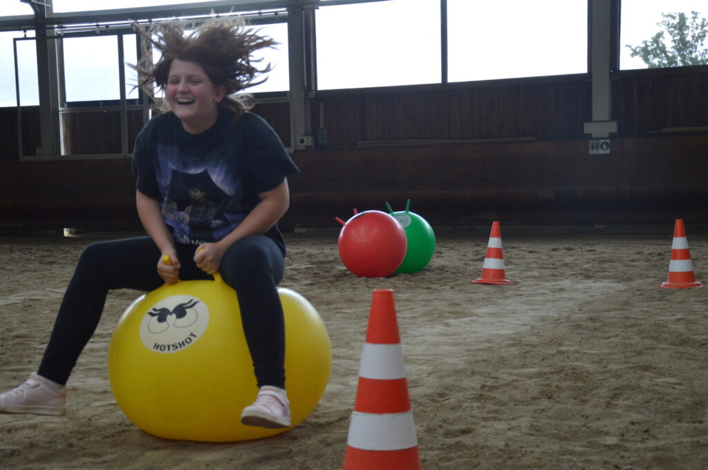 Jugendliche hüpft lachend auf einem gelben Hüpfball durch einen Parcours