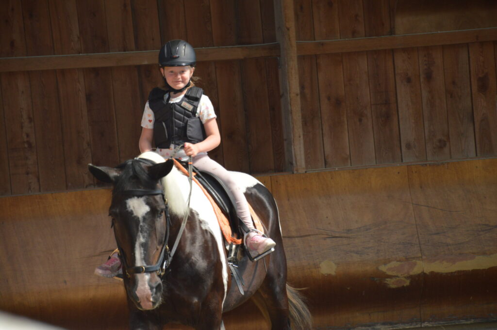 Mädchen mit Reithelm und Sicherheitsweste reitet auf einem dunklen Pony