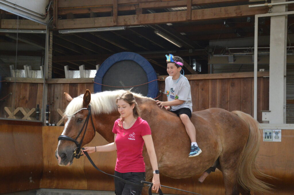 Junge reitet ohne Sattel auf einem Haflinger, eine Betreuerin führt das Pferd