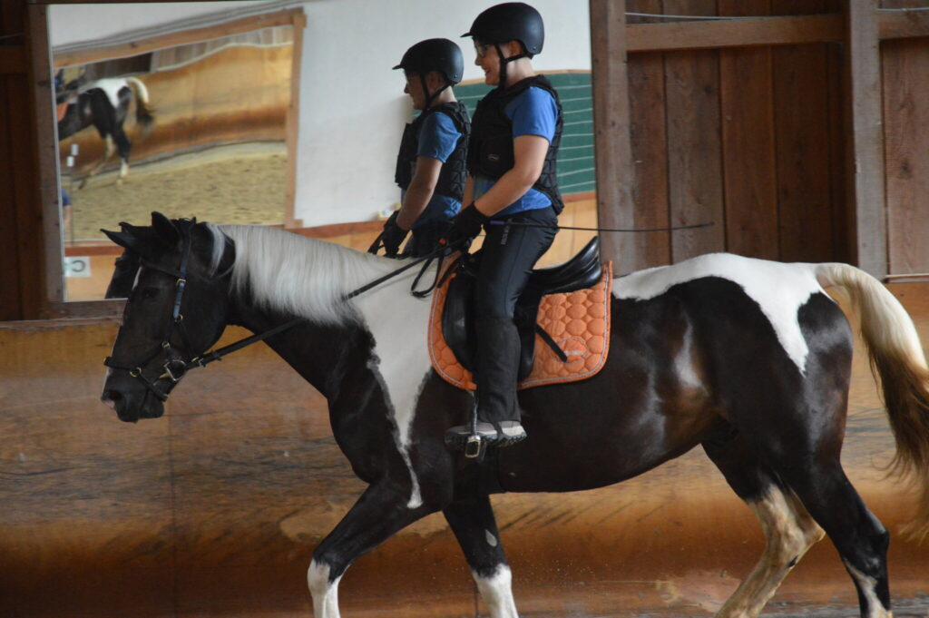 Zwei Kinder reiten gemeinsam auf einem schwarz-weiß gescheckten Pferd