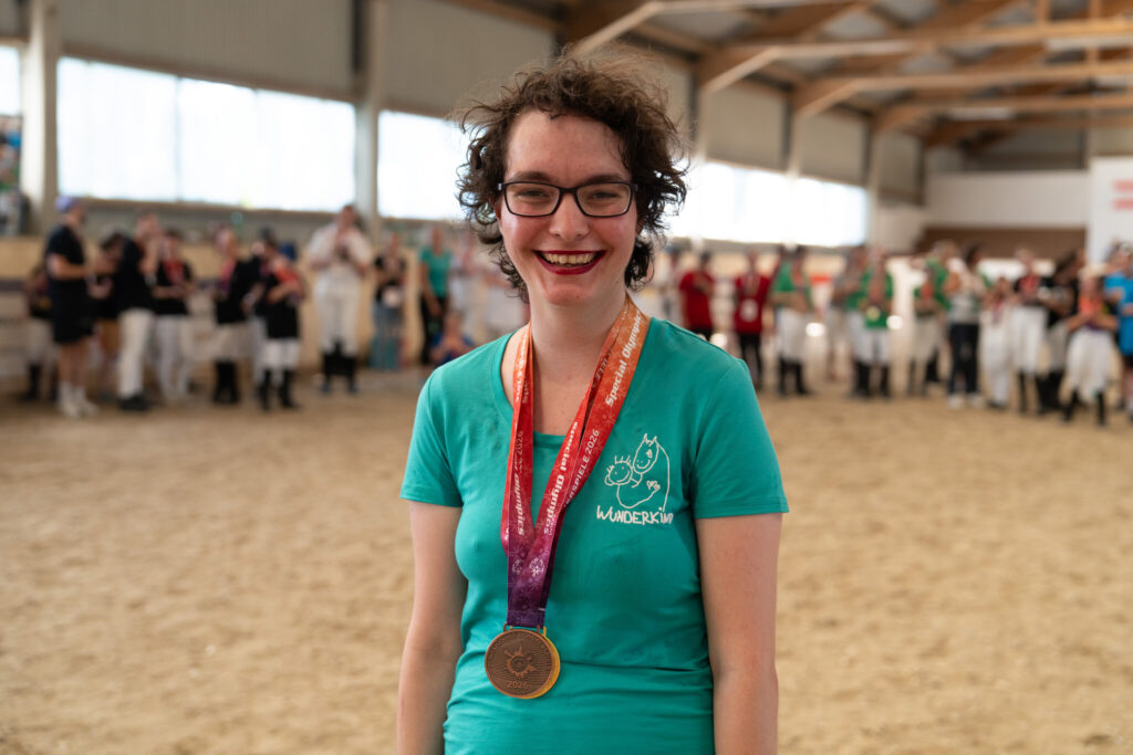 Athletin im türkisen Wunderkind-Shirt lächelt mit ihrer Goldmedaille in die Kamera