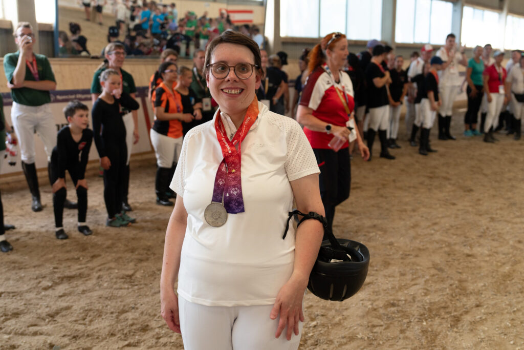 Athletin in weißer Turnierkleidung mit Medaille, den Reithelm in der Hand
