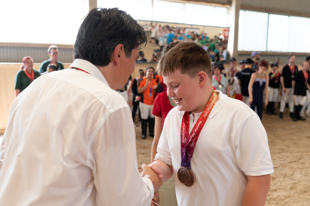 Junger Athlet erhält seine Bronzemedaille und schüttelt dabei die Hand