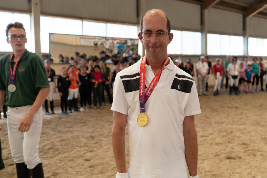 Zwei Athleten in der Reithalle, einer von beiden mit Goldmedaille um den Hals